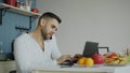 Handsome young man talking phone and using laptop computer sitting in the kitchen after breakfast in the morning Royalty Free Stock Photo