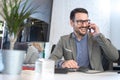 Handsome young man talking on smart phone and using computer while working in the office Royalty Free Stock Photo