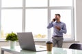 Handsome young man talking on smart phone and using computer while working in the office Royalty Free Stock Photo