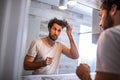 Handsome young man touching his hair with hand and grooming in bathroom at home. White metrosexual man worried for hair loss and Royalty Free Stock Photo
