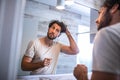 Handsome young man touching his hair with hand and grooming in bathroom at home. White metrosexual man worried for hair loss and Royalty Free Stock Photo