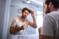 Handsome young man touching his hair with hand and grooming in bathroom at home. White metrosexual man worried for hair loss and Royalty Free Stock Photo