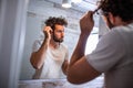 Handsome young man touching his hair with hand and grooming in bathroom at home. White metrosexual man worried for hair loss and Royalty Free Stock Photo