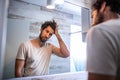 Handsome young man touching his hair with hand and grooming in bathroom at home. White metrosexual man worried for hair loss and Royalty Free Stock Photo