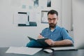 Handsome young man in trendy eyeglasses sits in his office while working on business project looks satisfied, takes Royalty Free Stock Photo