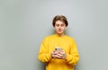 Handsome young man uses a smartphone on a gray wall background and listens to music. guy in the wireless headphones uses the Royalty Free Stock Photo