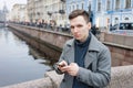 Handsome young man using mobile phone, wearing an elegant gray coat, stands Royalty Free Stock Photo
