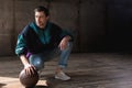 handsome young man in vintage windcheater with basketball ball sitting squats