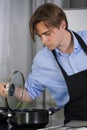 Handsome young man wearing an apron holding a lid and checking inside a pot Royalty Free Stock Photo