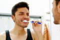 Handsome young man wearing black singlet top looking in mirror smiling while brushing teeth Royalty Free Stock Photo