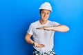 Handsome young man wearing builder uniform and hardhat gesturing with hands showing big and large size sign, measure symbol