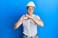 Handsome young man wearing builder uniform and hardhat smiling in love doing heart symbol shape with hands