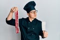 Handsome young man wearing chef uniform holding bacon and knife smiling looking to the side and staring away thinking Royalty Free Stock Photo