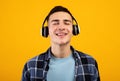 Handsome young man wearing headphones, listening to music with closed eyes on orange studio background Royalty Free Stock Photo