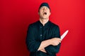 Handsome young man wearing professional cook uniform holding knife angry and mad screaming frustrated and furious, shouting with Royalty Free Stock Photo