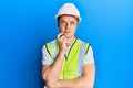 Handsome young man wearing safety helmet and reflective jacket serious face thinking about question with hand on chin, thoughtful