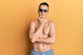 Handsome young man wearing swimsuit and sunglasses smiling looking confident at the camera with crossed arms and hand on chin Royalty Free Stock Photo