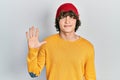 Handsome young man wearing wool hat showing and pointing up with fingers number five while smiling confident and happy