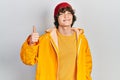 Handsome young man wearing yellow raincoat smiling happy and positive, thumb up doing excellent and approval sign Royalty Free Stock Photo