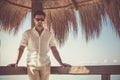 Handsome young man with white shirt and sunglasses relaxed leaning on a wooden bar. During the summer, with reed leaves in the Royalty Free Stock Photo