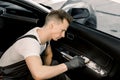 Handsome young man, worker of professional car detailing workshop, washing car door interior by a soft brush with foam Royalty Free Stock Photo