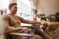 Handsome young man working in cafe with a dog, sitting on chair and using laptop, petting his golden retriever in animal Royalty Free Stock Photo