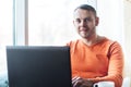 Handsome young man working on notebook, smiling, looking at camera, while enjoying coffee in cafe Royalty Free Stock Photo