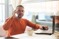 Handsome young man working with notebook, talking on the phone, looking at camera, while enjoying coffee in cafe