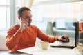 Handsome young man working with notebook, talking on the phone, smiling, while enjoying coffee in cafe Royalty Free Stock Photo