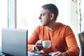 Handsome young man working on notebook, thinking, looking out the window, while enjoying coffee in cafe Royalty Free Stock Photo