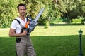 Handsome young man in working outfit equipment with an electric circular chainsaw in his hands on a green background with a countr Royalty Free Stock Photo