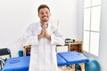 Handsome young man working at pain recovery clinic praying with hands together asking for forgiveness smiling confident Royalty Free Stock Photo
