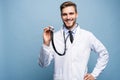 Handsome young medic holding a stethoscope, isolated over light blue.