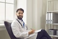 Handsome young medical doctor in lab coat sitting at hospital. Medical worker writing prescription form at office Royalty Free Stock Photo