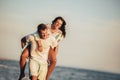 Young man giving piggyback ride to girlfriend on beach. Young couple enjoying summer holidays Royalty Free Stock Photo