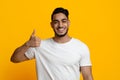 Handsome young middle eastern guy showing thumb up on yellow