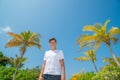 Handsome young model man wearing white t-shirt standing at sandy beach at tropical island luxury resort