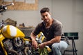 A handsome young motorcyclist in jeans and a t-shirt poses for a photo sitting on a bike in his garage