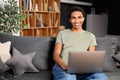 Handsome young multiracial man with beard sitting on the sofa with laptop at home, searching in the internet, watching Royalty Free Stock Photo