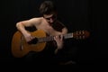 Handsome young musician playing on guitar. Naked torso. On black background