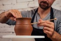 Handsome young potter man in a gray sweater and a black apron sculpts clay pot on a potter`s wheel in a cozy craft Royalty Free Stock Photo