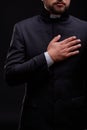 Handsome young priest with bread posing on a black background.