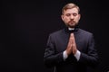 Handsome young priest with bread posing on a black background.