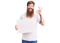 Handsome young red head man with long beard holding blank empty banner doing ok sign with fingers, smiling friendly gesturing Royalty Free Stock Photo