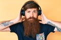 Handsome young red head man with long beard listening to music using headphones relaxed with serious expression on face Royalty Free Stock Photo