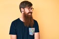 Handsome young red head man with long beard wearing casual clothes and glasses looking away to side with smile on face, natural Royalty Free Stock Photo