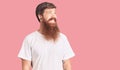 Handsome young red head man with long beard wearing casual white tshirt looking away to side with smile on face, natural Royalty Free Stock Photo