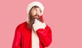 Handsome young red head man with long beard wearing santa claus costume with hand on chin thinking about question, pensive Royalty Free Stock Photo