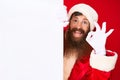 Handsome young red head man with long beard wearing santa claus costume holding banner doing ok sign with fingers, smiling Royalty Free Stock Photo