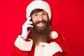 Handsome young red head man with long beard wearing santa claus costume talking on the phone pointing finger to one self smiling Royalty Free Stock Photo